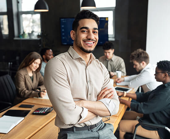 A smiling man stands in front of a conference room table where a group of people is working
