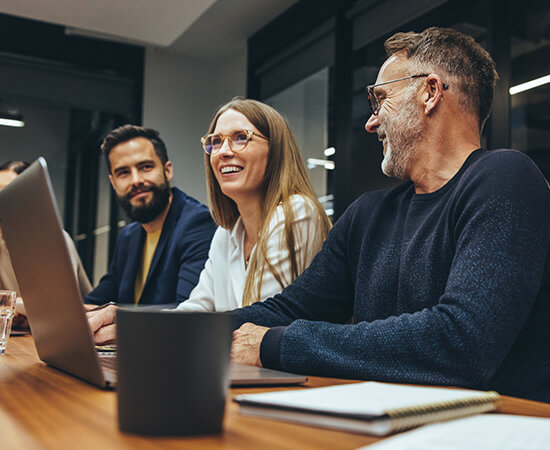 Three smiling people sitting at a table using laptops